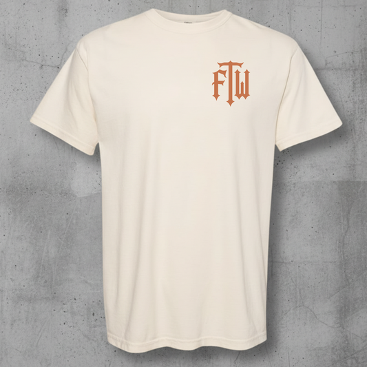 An off-white crewneck t-shirt with a small orange gothic-style 'ftw' logo on the left chest, displayed against a textured gray concrete background.