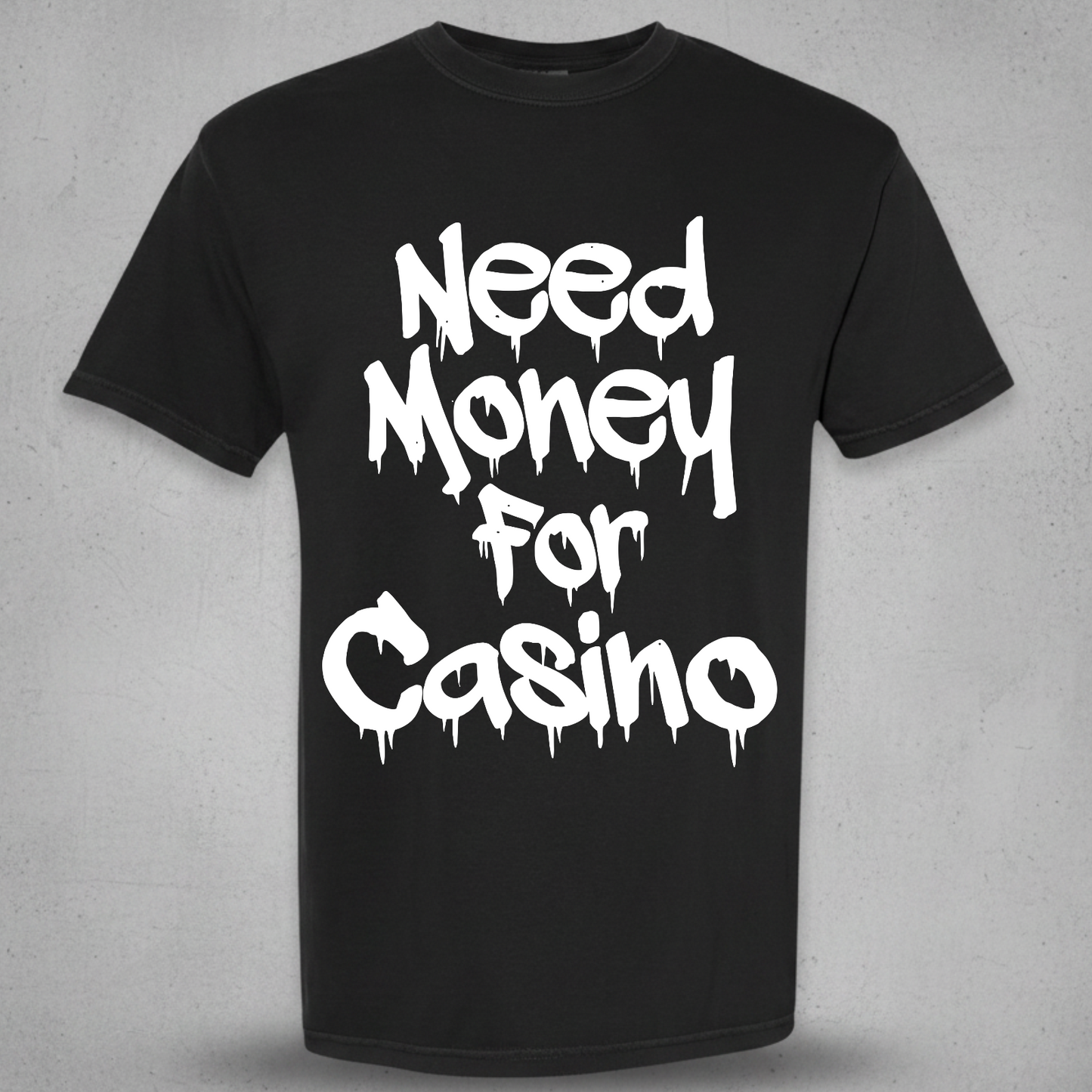 A black short-sleeve crewneck t-shirt with the phrase 'Need Money For Casino' printed in a white dripping graffiti-style font on the front, displayed against a textured gray background.