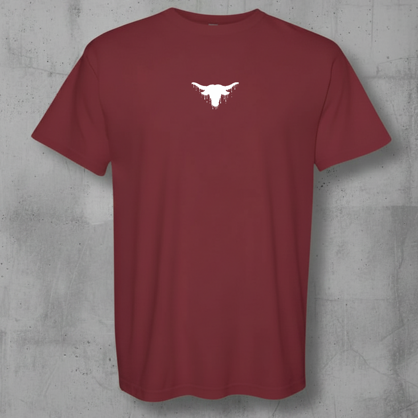 A short-sleeve crewneck t-shirt in maroon with a small white longhorn steer graphic centered on the chest, displayed against a textured gray concrete wall.