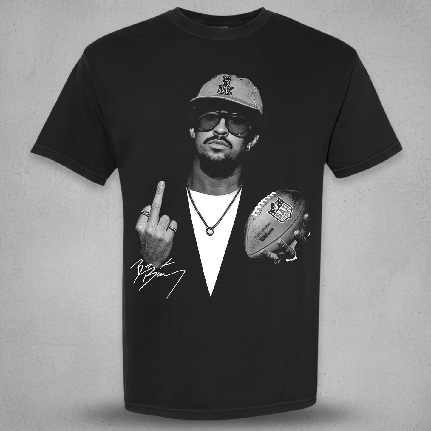 A black short-sleeve graphic t-shirt featuring a black and white print of a man wearing a cap and sunglasses, holding a football and making a middle finger gesture, with a signature graphic below. The t-shirt is displayed against a textured gray background.