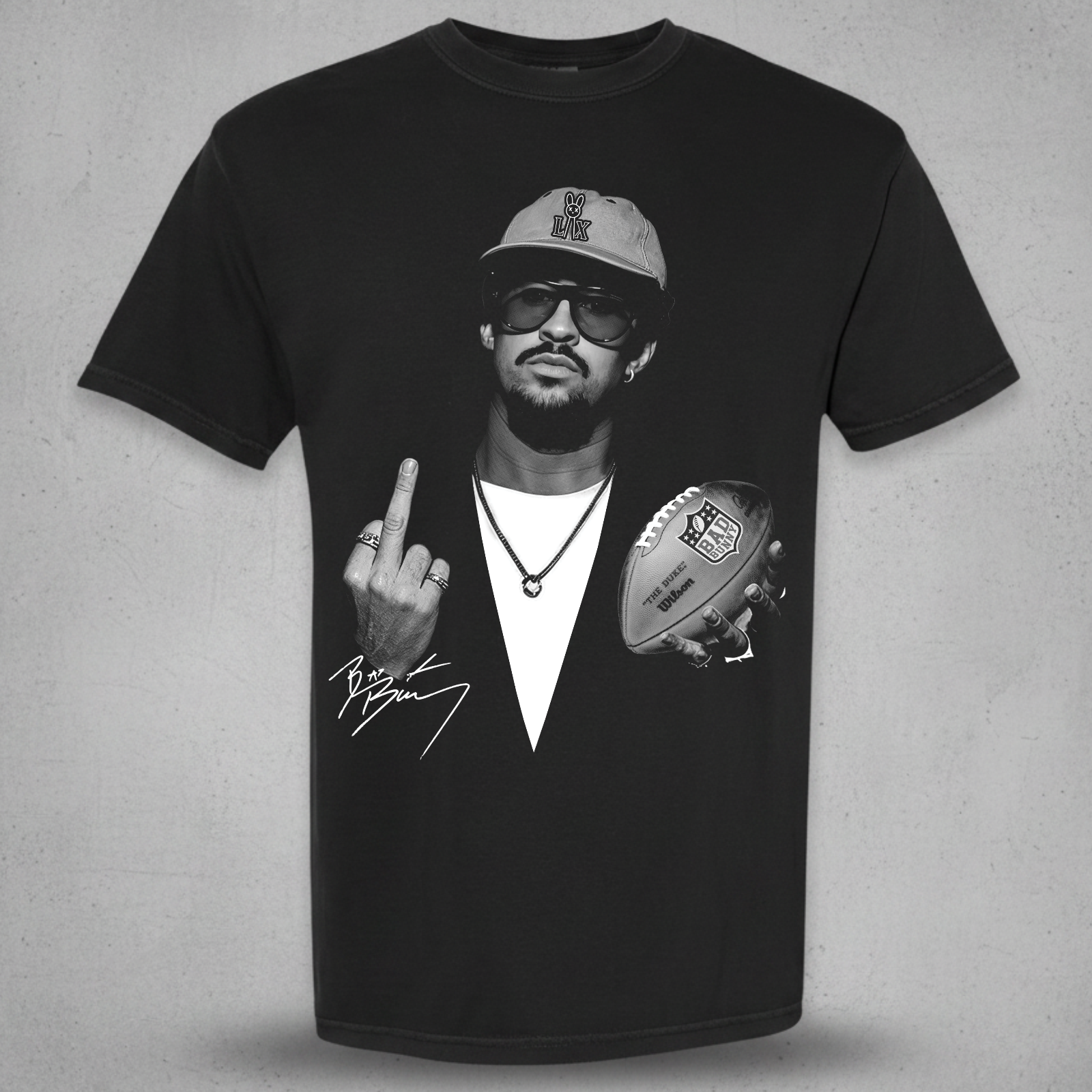 A black short-sleeve graphic t-shirt featuring a black and white print of a man wearing a cap and sunglasses, holding a football and making a middle finger gesture, with a signature graphic below. The t-shirt is displayed against a textured gray background.