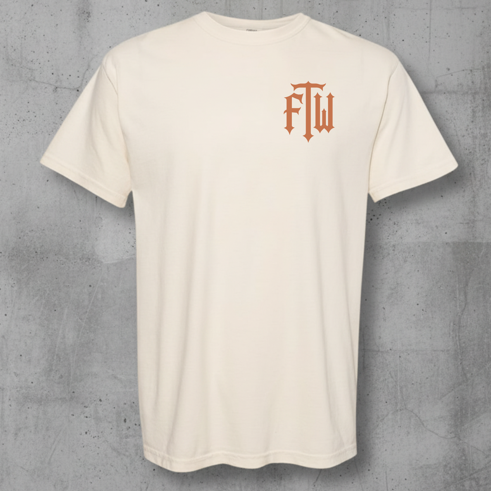 An off-white crewneck t-shirt with a small orange gothic-style 'ftw' logo on the left chest, displayed against a textured gray concrete background.