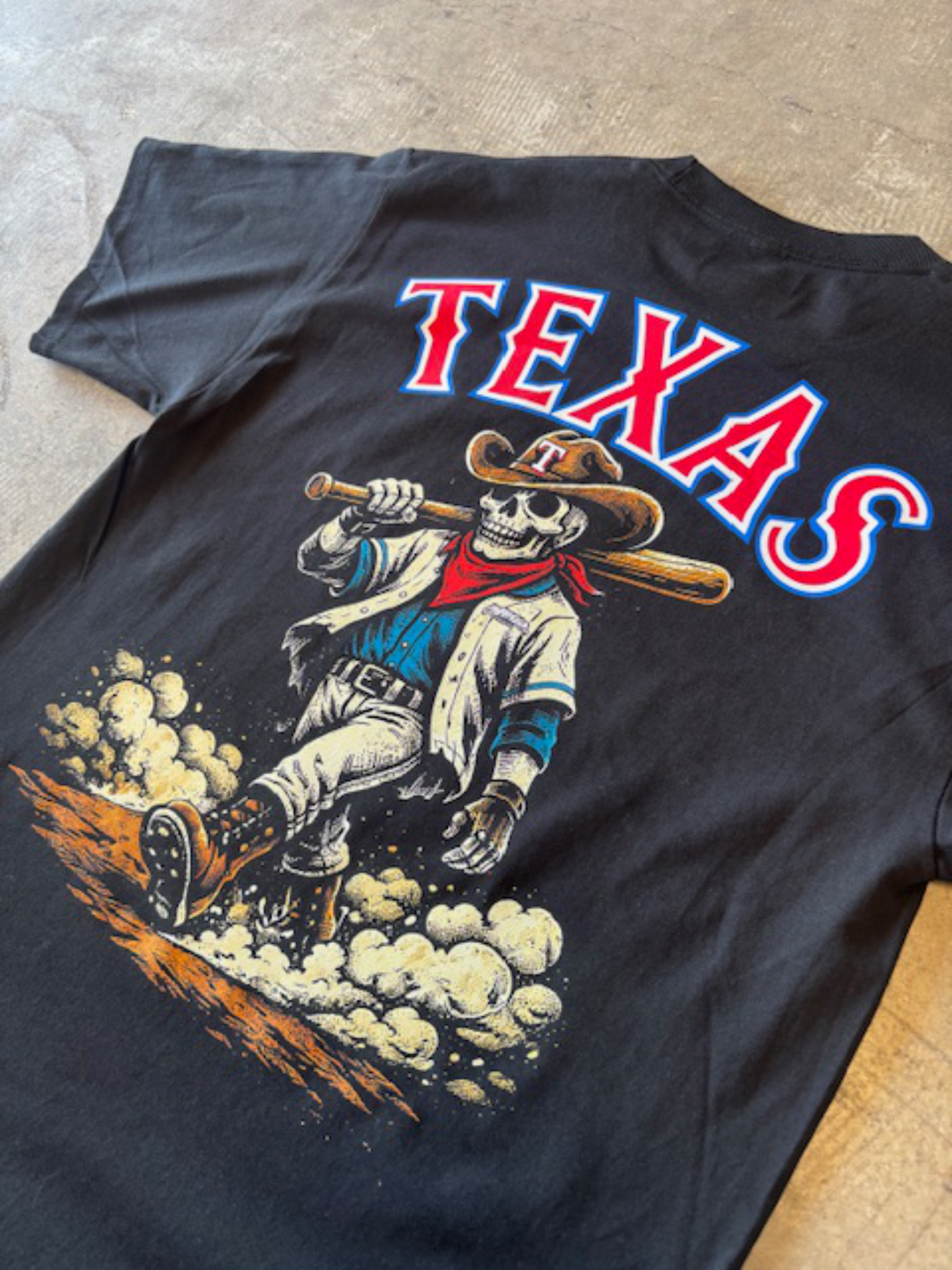 Black t-shirt with a graphic of a skeleton cowboy and 'TEXAS' text on a concrete floor.