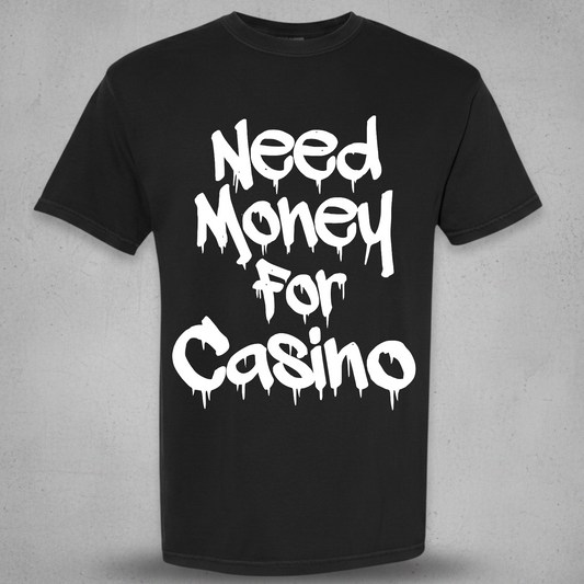 A black short-sleeve crewneck t-shirt with the phrase 'Need Money For Casino' printed in a white dripping graffiti-style font on the front, displayed against a textured gray background.