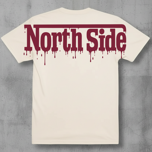 An off-white t-shirt with a dark red dripping 'North Side' graphic across the chest, displayed flat against a textured gray concrete background.