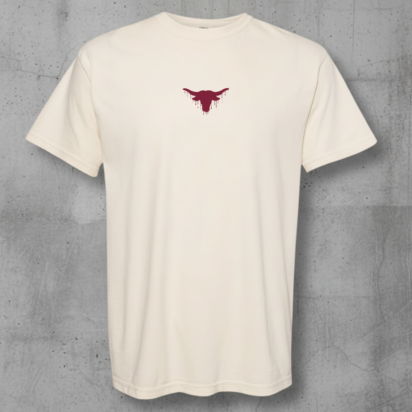 An off-white short-sleeve crewneck t-shirt with a small dark red bull graphic on the center chest, displayed against a textured gray concrete wall.