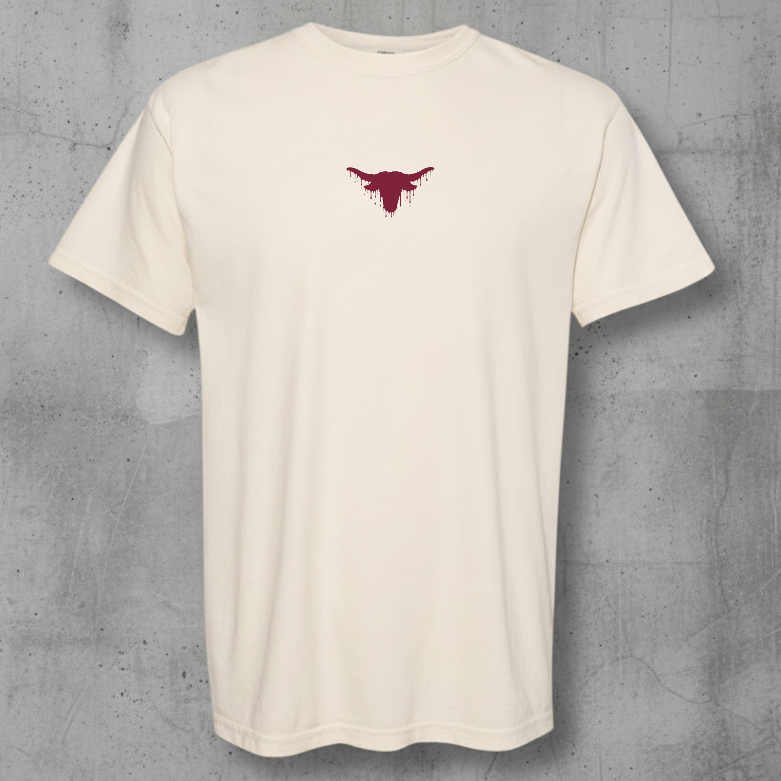 An off-white short-sleeve crewneck t-shirt with a small dark red bull graphic on the center chest, displayed against a textured gray concrete wall.