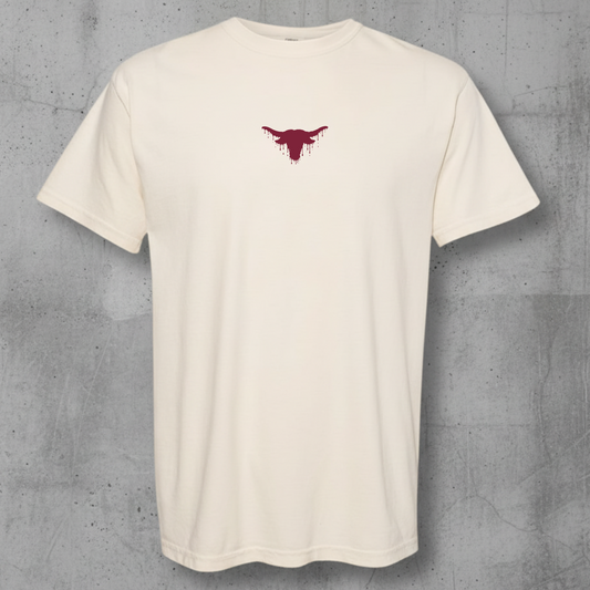 An off-white short-sleeve crewneck t-shirt with a small dark red bull graphic on the center chest, displayed against a textured gray concrete wall.