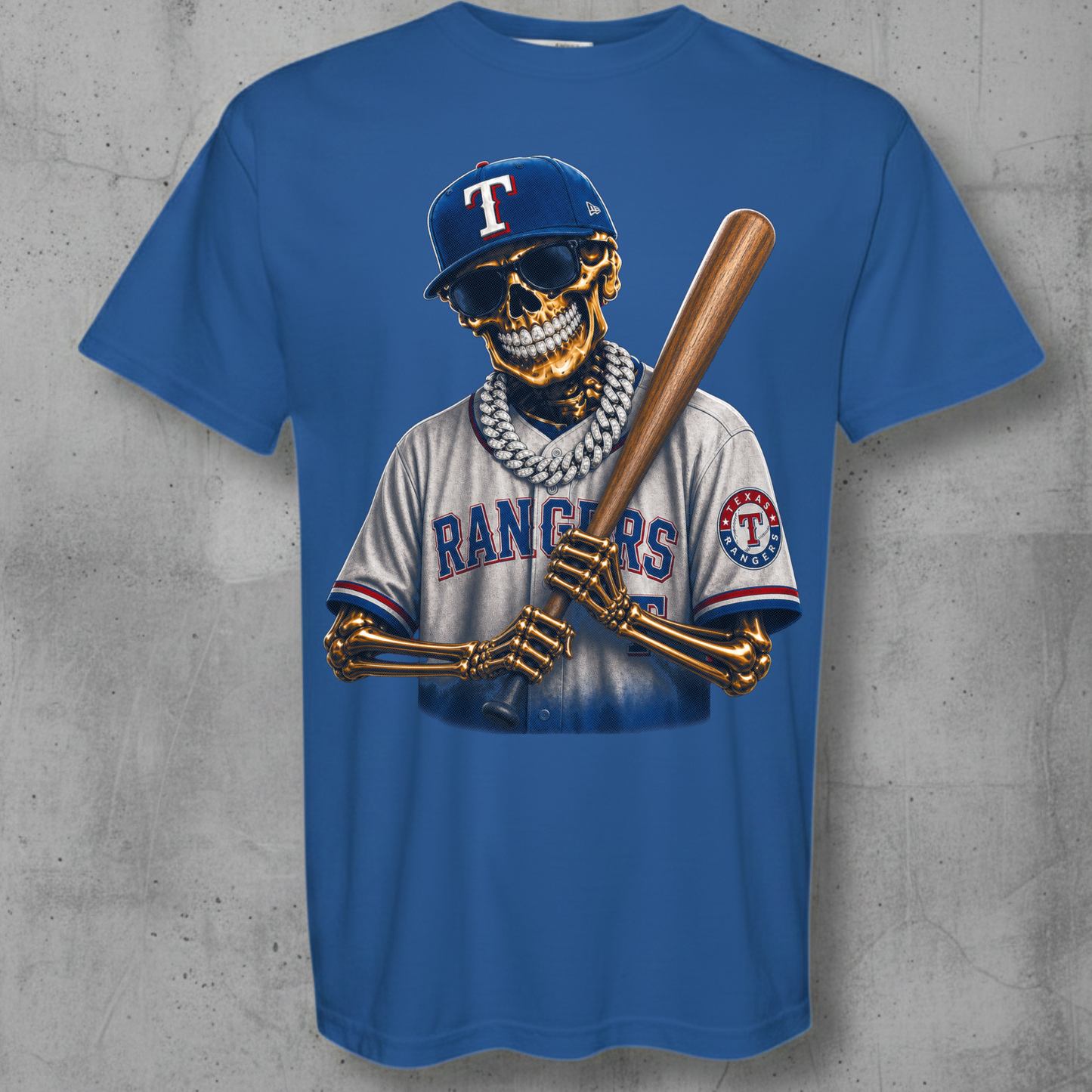 A blue short-sleeve graphic t-shirt featuring a cartoon baseball player skeleton wearing a Texas Rangers uniform and holding a bat, displayed against a textured gray concrete wall.