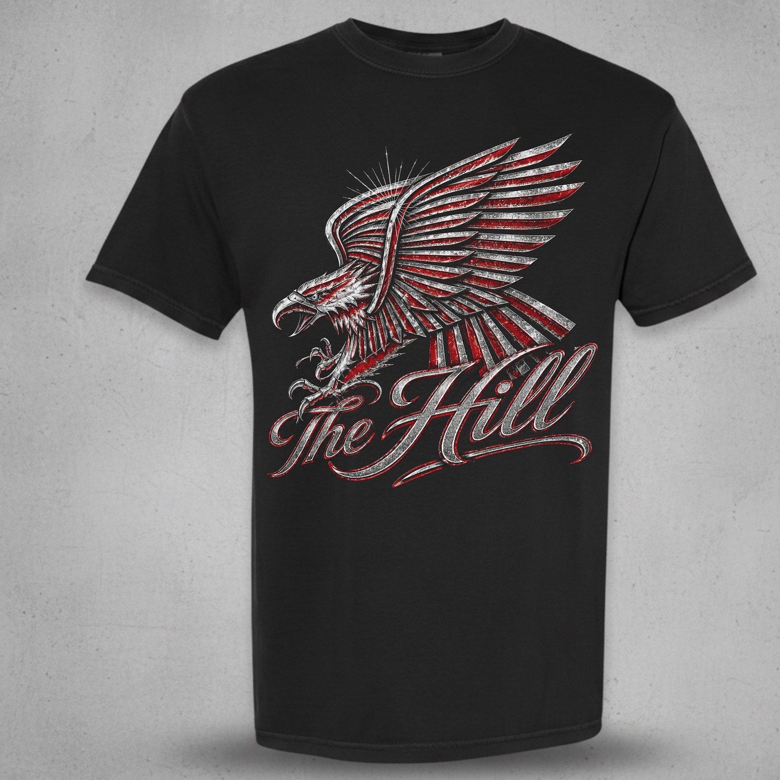 A black short-sleeve t-shirt with a distressed graphic of an eagle with red and white feather details and the words 'The Hill' in red and white script, displayed on a textured gray background.
